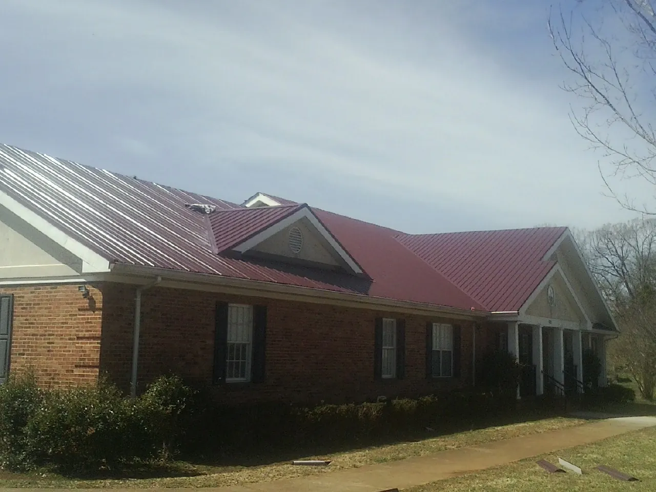 Red metal roof with gabled entries on a long brick building, from a Hail Damage Roof Repair job in Buford