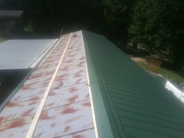 Old rusted panels beside newly installed green metal roofing — Wind Damage Roof Repair by Roofing Brothers in Buford